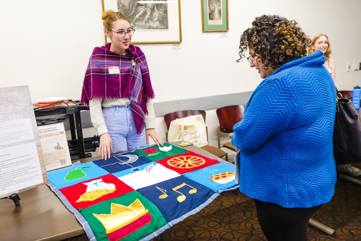 A woman wearing a purple shawl shows a colorful quilt to a person wearing a dark blue coat. Photo by Ashley Sorensen/ASU.