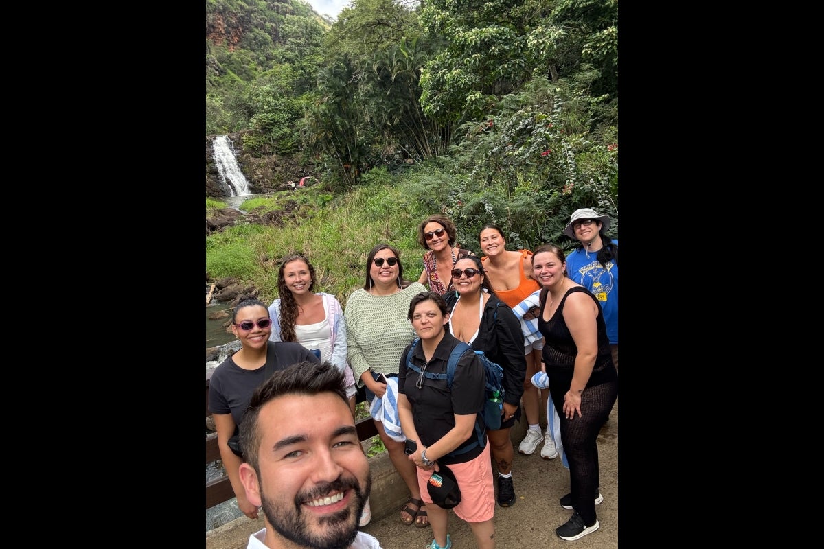 A group of people pose for a photo in front of a rainforest waterfall.