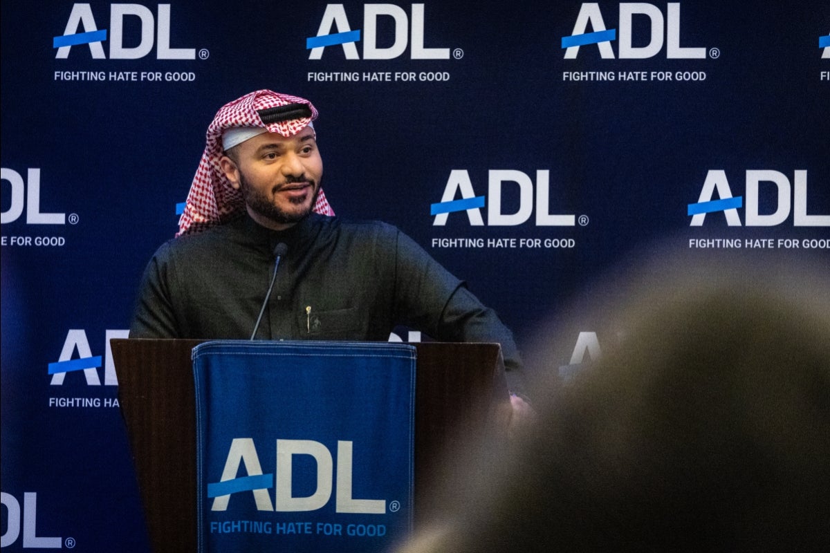 Man wearing a black Islamic robe and head covering speaks at a lectern in front of an audience