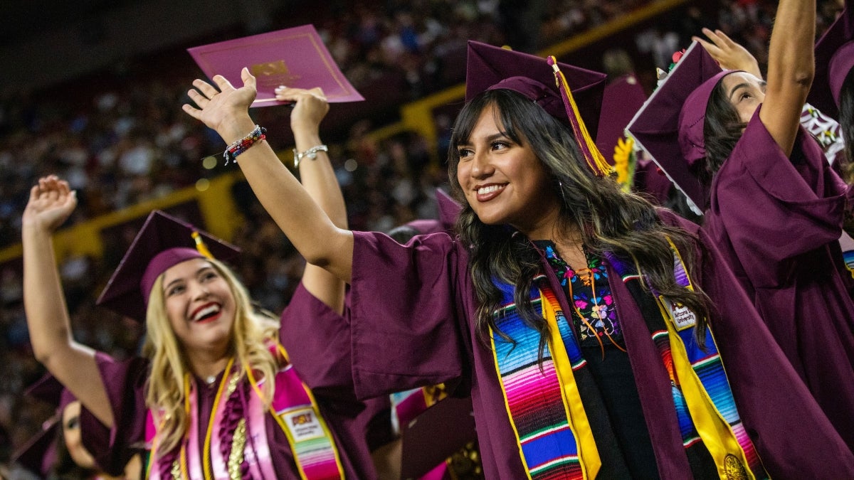 Women in graduation caps and gowns wave at their families
