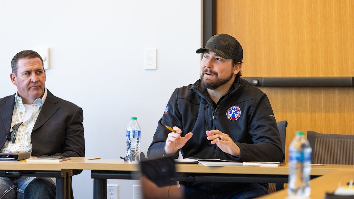 Man seated at a table speaking to a room of unseen veterans.