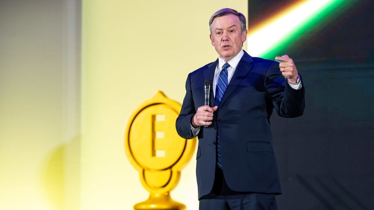 Man in a suit with a blue tie speaks on stage at award ceremony
