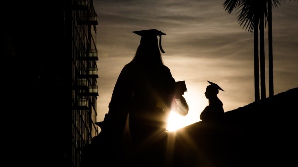 Graduates are silhouetted against the setting sun