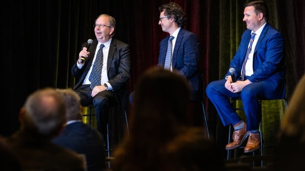 Three men in suits and ties sit on stage talking to audience