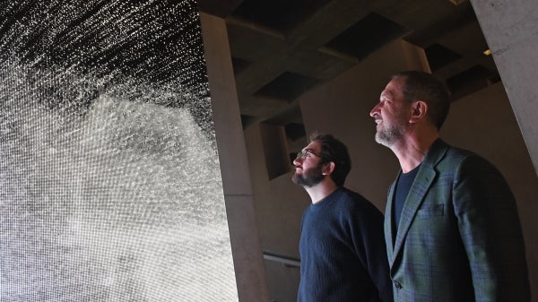 Two men gaze upon a screen displaying points of moving white light.