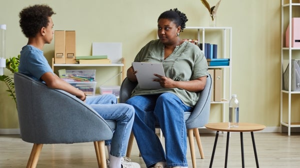 Two people seated facing each other and talking while one holds a clipboard.