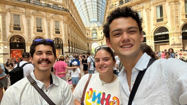 Three people pose for a photo in a public place in Italy with a crowd of people around them