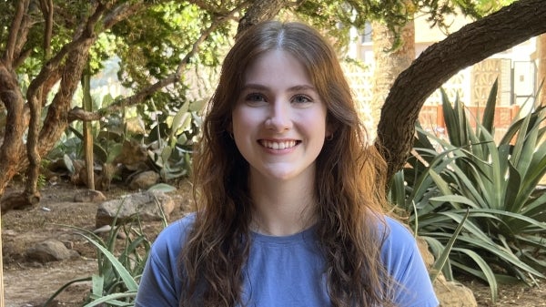 A woman with brown hair and a blue shirt smiles at the camera in a desert garden.