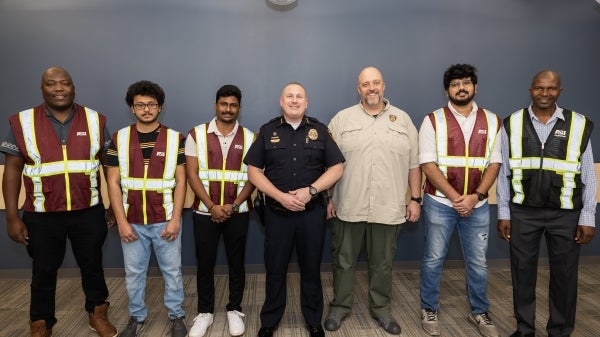 Seven people stand in a line smiling, a police officer in the middle and others wearing safety vests