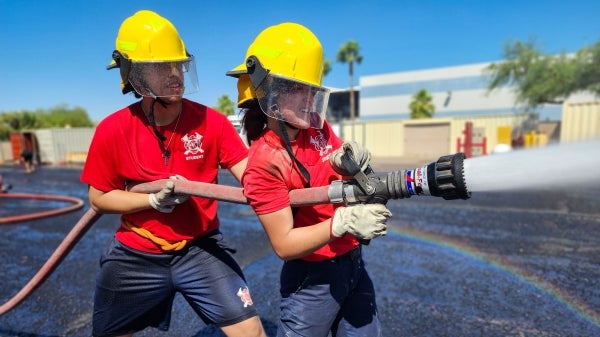 Two students hold a fire hose that is spraying water