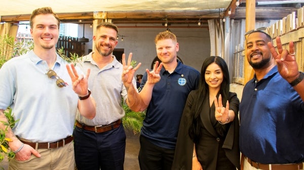 Five people pose for a photo while holding up the pitchfork gesture.