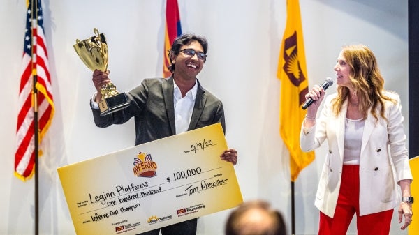 A young man holds up a trophy and a large check