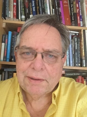 Courtesy photo of ASU Associate Professor Joe Lockard, who poses in front of his home bookshelves.